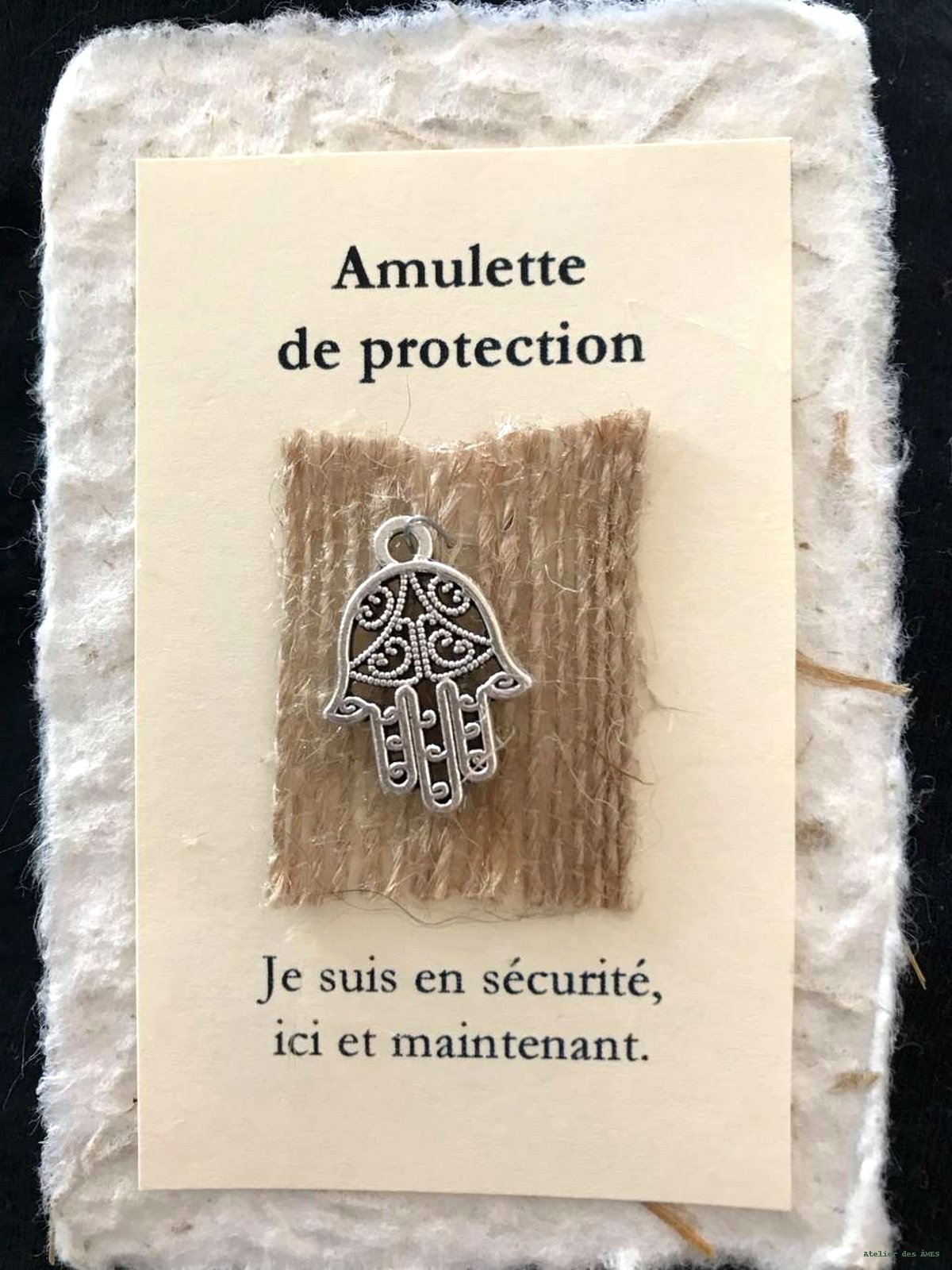 Amulette de protection — main argentée sur toile de jute, carte crème